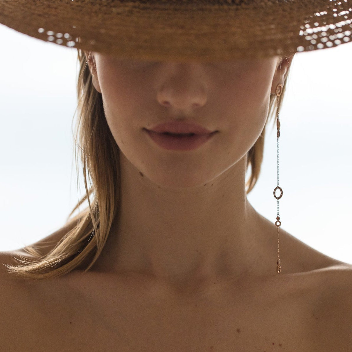 Close-up of a person wearing a straw hat and long earrings asymmetric against a sea background